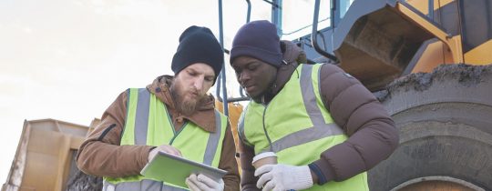 Men looking at tablet next to construction machinery